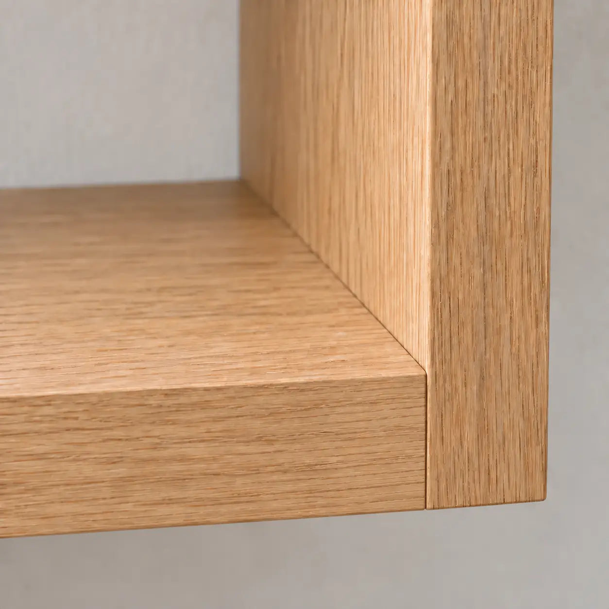 Close-up of a light oak floating bathroom vanity corner showing the grain texture and beveled edge against a neutral light gray background.