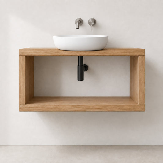 A modern floating vanity with a light oak wood frame and open shelf, holding a white vessel sink with two matte silver wall-mounted faucets, set against a warm beige wall.