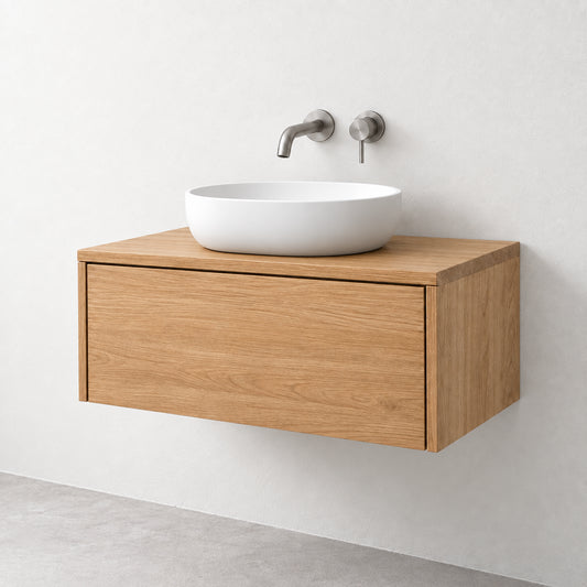 A modern floating bathroom vanity with a light oak wood cabinet, a white ceramic vessel sink, and a brushed nickel wall-mounted faucet against a white wall.