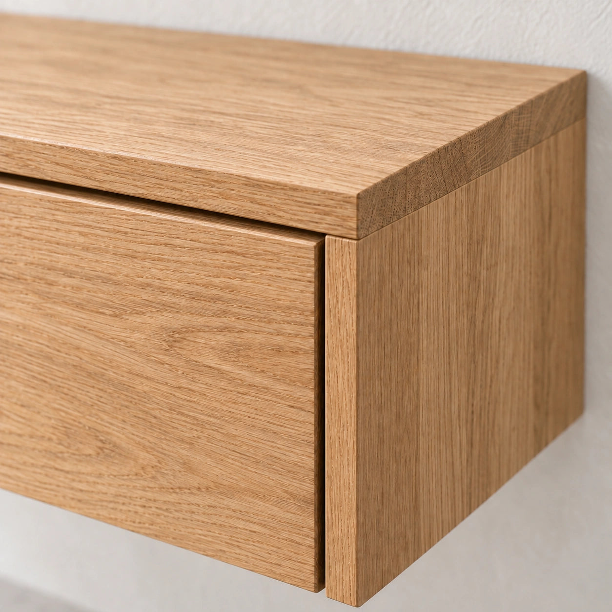 Close-up of a light oak wood wall-mounted cabinet or drawer front with visible wood grain and a clean modern edge profile against a white wall.