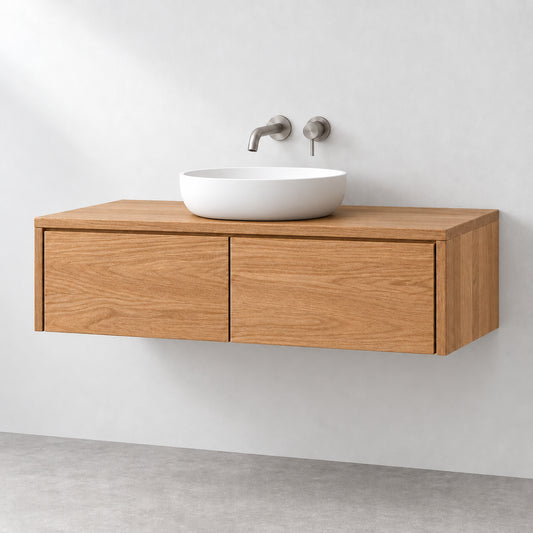 A modern floating bathroom vanity made of light oak wood with two drawers, mounted on a white wall above a gray floor, featuring a white ceramic vessel sink and brushed metal wall-mounted faucets.