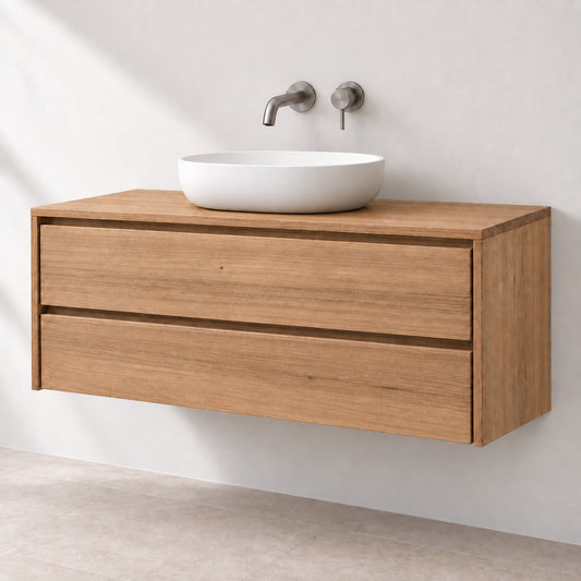 A modern floating bathroom vanity made of light oak wood, featuring two drawers and a white ceramic vessel sink with a matte chrome wall-mounted faucet and controls, set against a textured off-white wall.