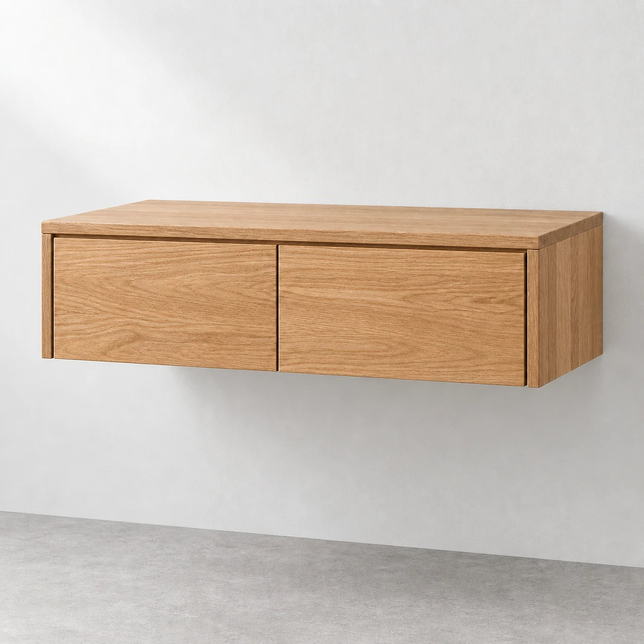 A modern floating wall cabinet with a light oak wood finish, featuring two large drawers and a minimalist design, mounted on a light gray wall above a concrete floor.